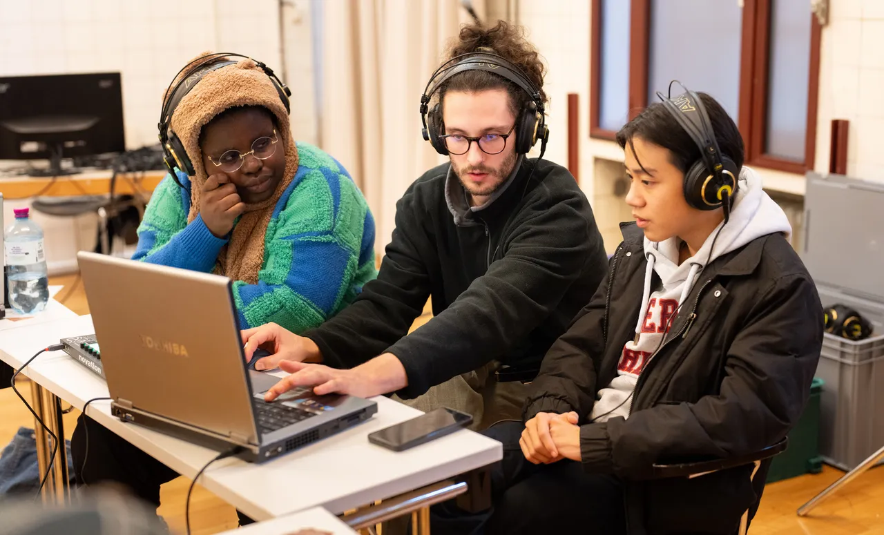 Drei Jugendliche mit Kopfhörern arbeiten gemeinsam an einem Laptop, um Sounds zu entwickeln.