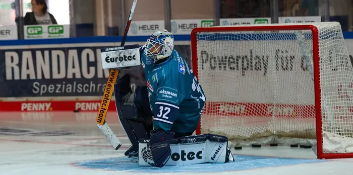 Eishockey-Torwart Hendrik Hane in blauem Trikot kniet mit Schläger und Schutzausrüstung vor dem Tor auf dem Eis.