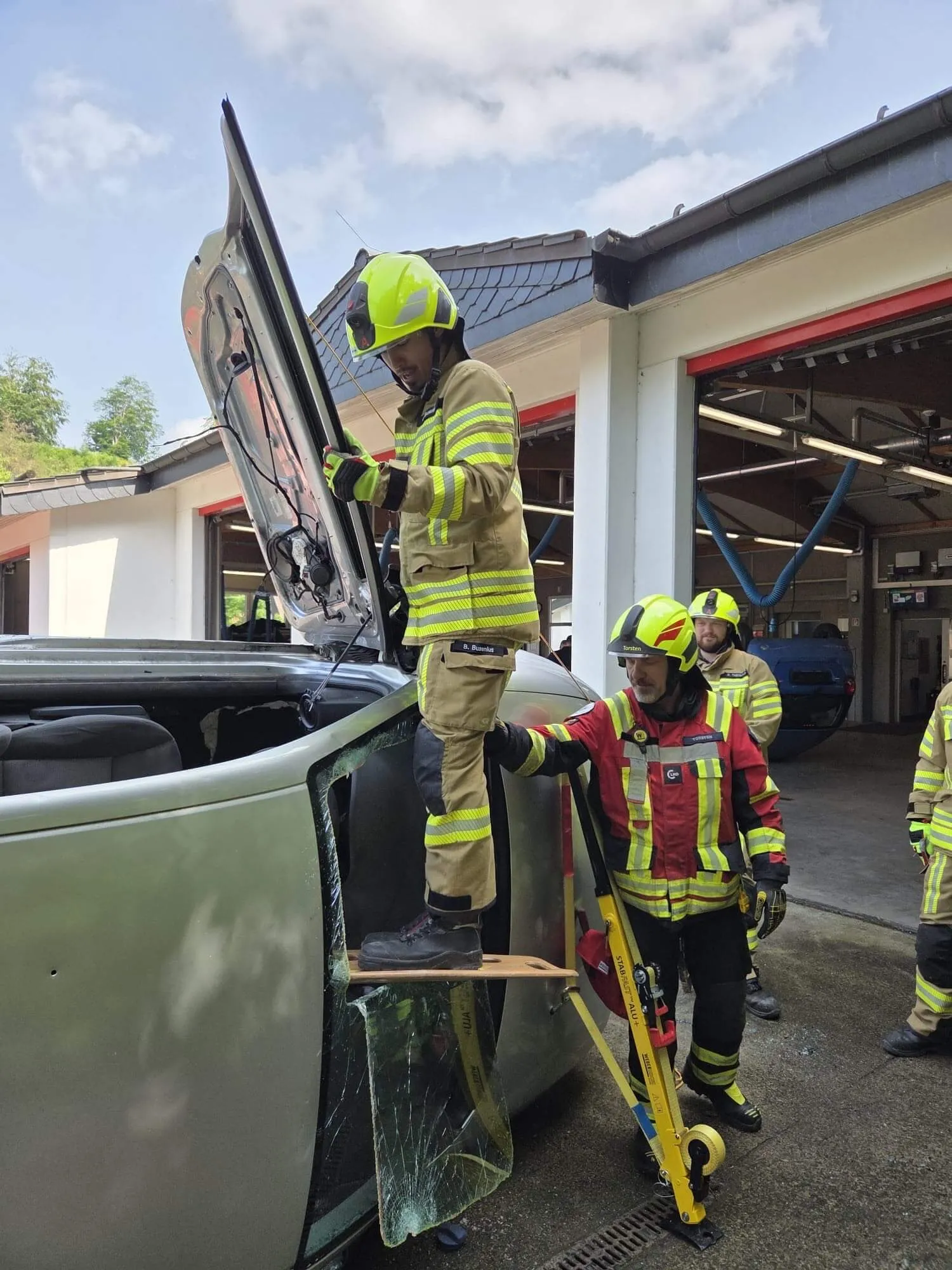 Feuerwehrleute bergen eine Person aus einem stark beschädigten Auto. Ein Retter steht auf dem Dach des Wagens, während ein Kollege ihn sichert.