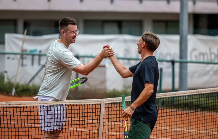 Zwei Tennisspieler schütteln sich auf einem Sandplatz die Hände über dem Netz.