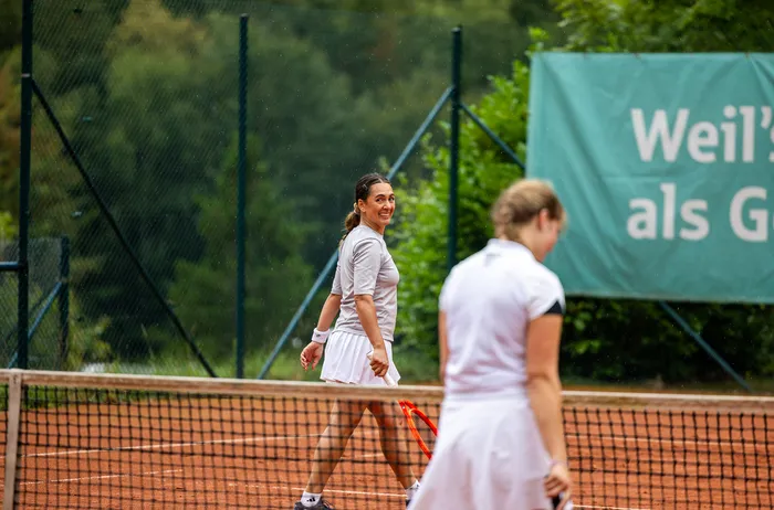 Eine lächelnde Tennisspielerin in weißer Kleidung läuft über einen Sandplatz.
