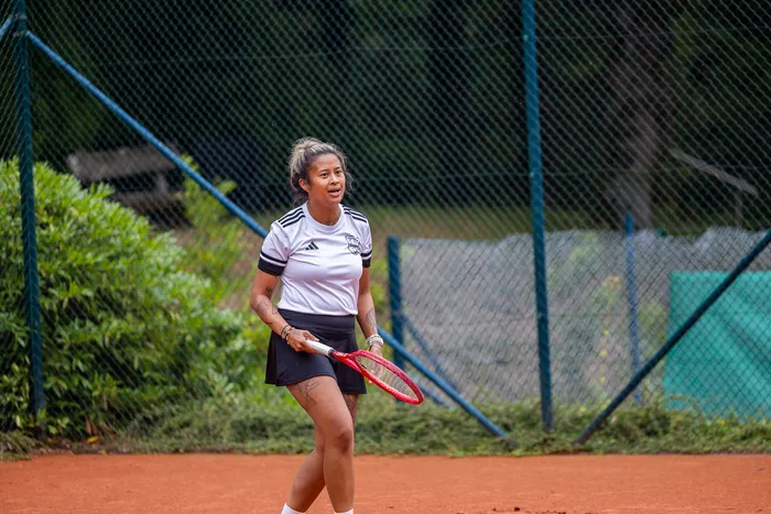 Eine Tennisspielerin in weißem Trikot und schwarzem Rock steht mit einem roten Schläger auf einem Sandplatz.