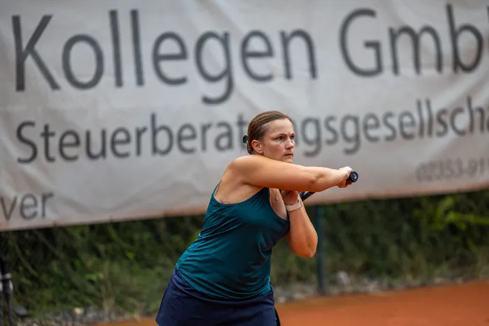 Eine Tennisspielerin bereitet auf einem Sandplatz einen Schlag vor, im Hintergrund ist ein Werbebanner zu sehen.