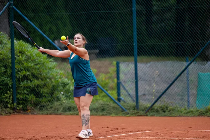 Eine Tennisspielerin wirft einen gelben Ball für den Aufschlag in die Luft auf einem Sandplatz.