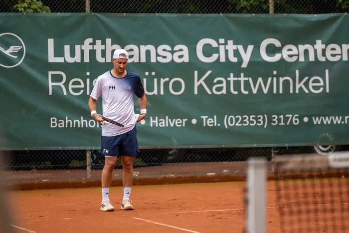 Ein Tennisspieler in weißem T-Shirt und blauen Shorts steht auf einem Sandplatz vor einem grünen Werbebanner der Lufthansa City Center.