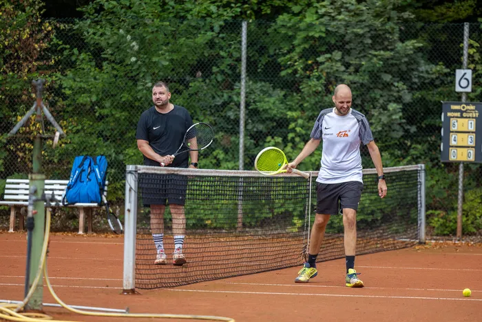 Zwei Männer stehen auf einem Sandplatz bei einem Tennisturnier, einer hinter dem Netz und einer davor mit einem hellgrünen Schläger.