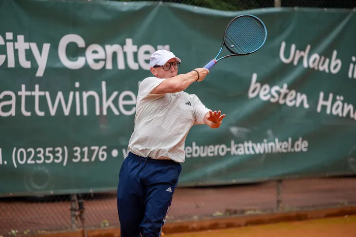 Ein Mann in weißem T-Shirt und blauer Hose schwingt einen Tennisschläger bei einem Spiel der MTC/TC Halver Open.