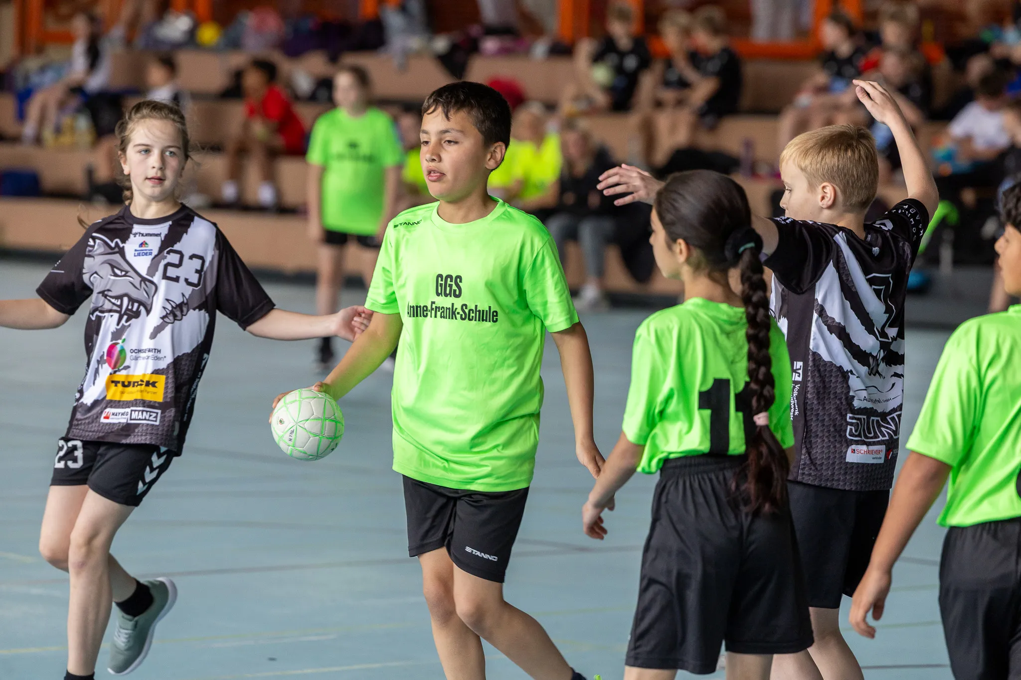 Junge Handballspieler in grünen und schwarzen Trikots während eines Spiels in einer Sporthalle. Ein Spieler hält den Ball.