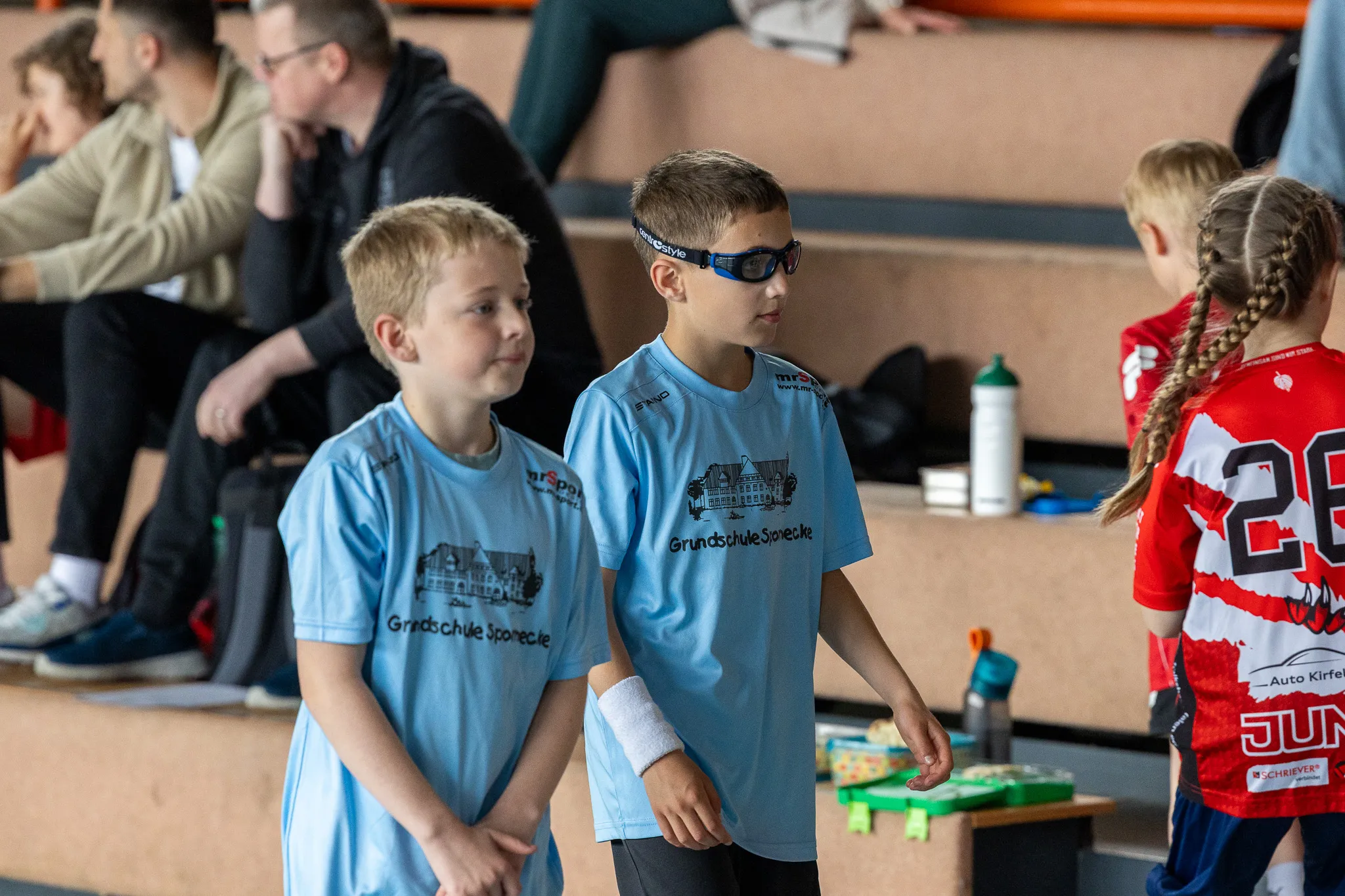 Drei Jungen in blauen Trainingsanzügen mit dem Aufdruck „Grundschule Sponecke“ stehen nebeneinander in einer Sporthalle.