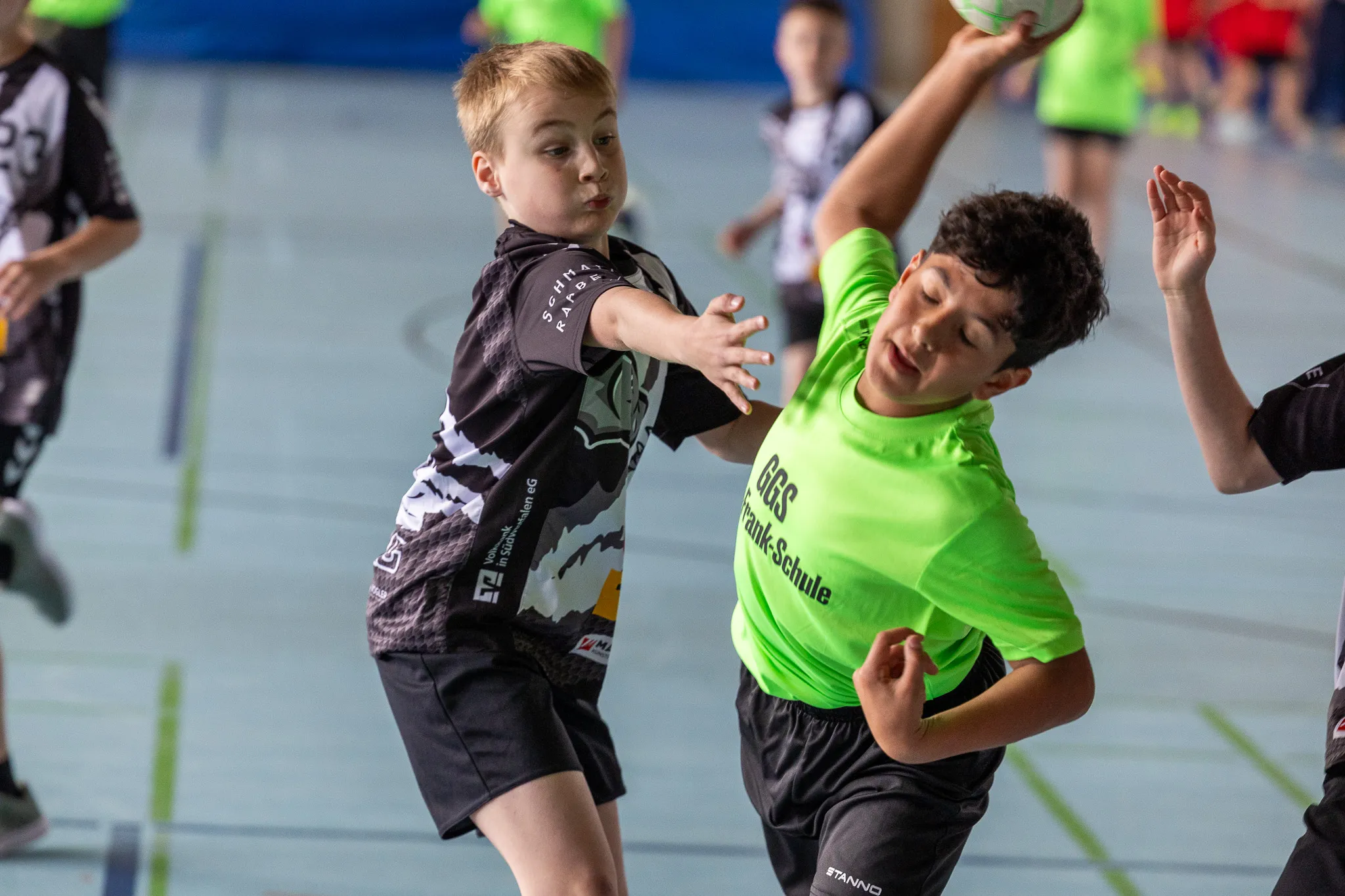 Zwei Jungen beim Handballspiel in einer Sporthalle. Der Junge im schwarzen Trikot wirft den Ball, während der andere ihn fängt.