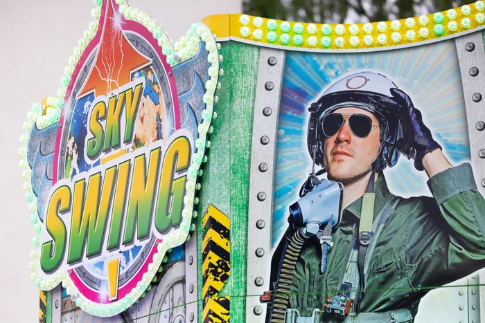 Werbung für den „Sky Swing“-Fahrgeschäft mit einem Mann in Pilotenmontur und Sonnenbrille.