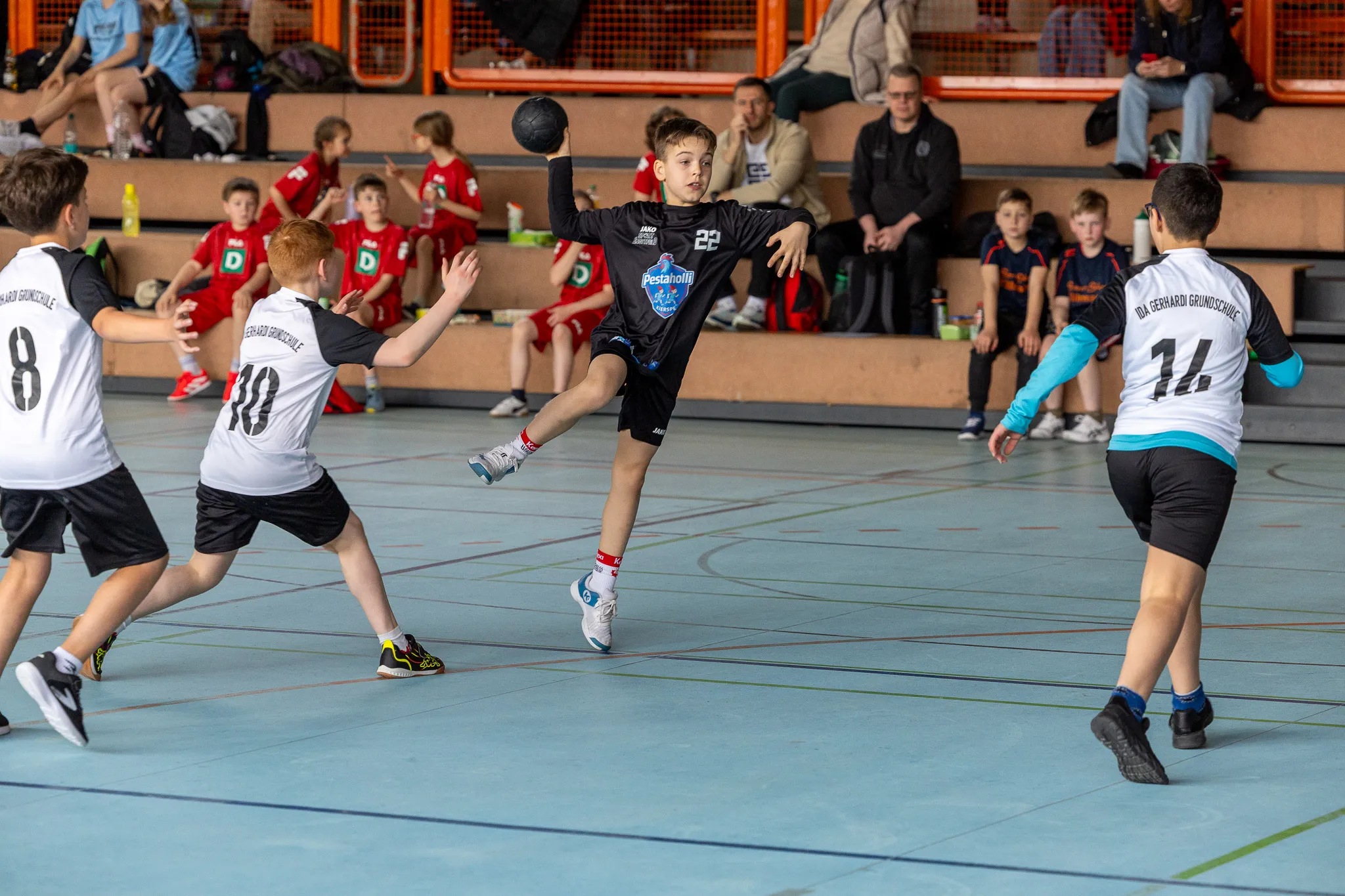 Handballspieler in blauen und schwarzen Trikots während eines Spiels in einer Sporthalle. Im Hintergrund Zuschauer auf den Tribünen.