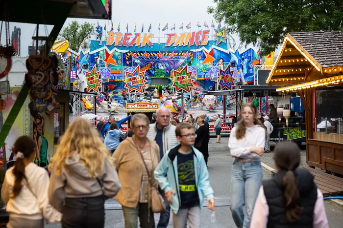 Menschenmengen bewegen sich vor einer bunt beleuchteten Fahrgeschäftskulisse auf der Kirmes in Halver.