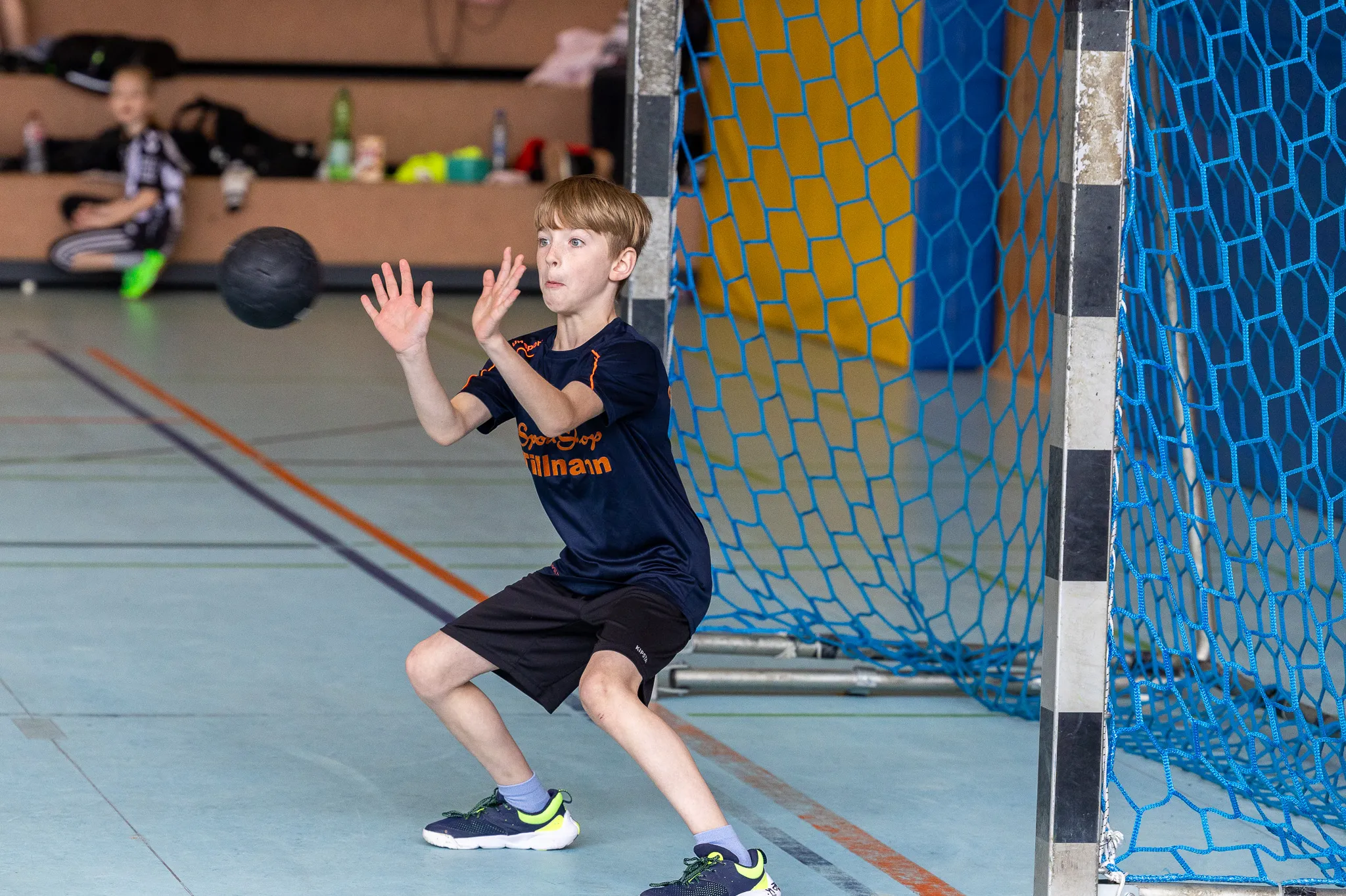 Ein Jugendlicher in Sportkleidung springt beim Handball in einer Sporthalle in die Höhe, um den Ball zu fangen.