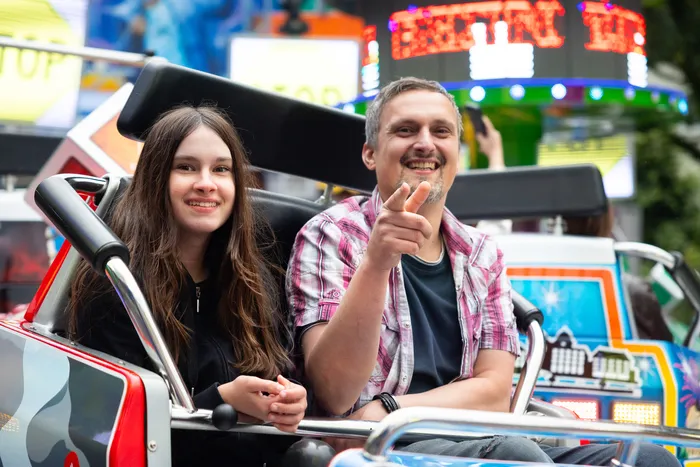 Vater und Tochter lächeln in einem Fahrgeschäft auf der Kirmes, der Mann zeigt mit dem Finger nach vorne.