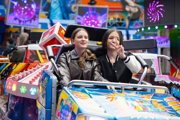 Zwei junge Frauen sitzen lachend in einer Karussell-Gondel auf der Kirmes.