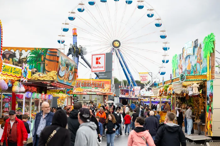 Volksfest mit Riesenrad und vielen Besuchern. Im Hintergrund ein Supermarktlogo.