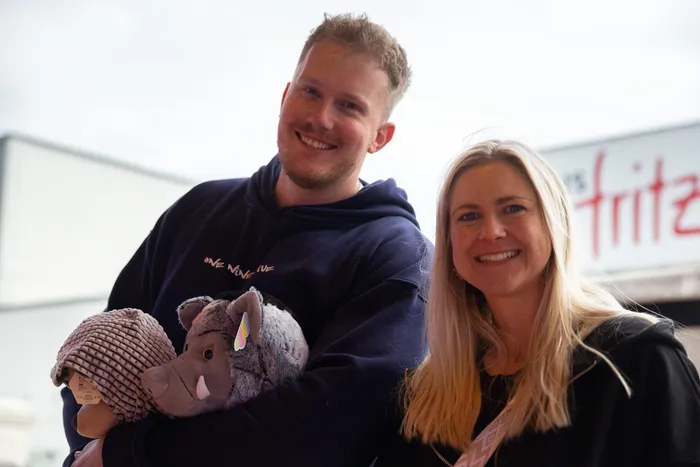 Ein Mann und eine Frau lächeln in die Kamera, während der Mann ein Wildschwein-Maskottchen hält. Im Hintergrund ist ein Kirmesstand mit der Aufschrift „fritz“ zu sehen.