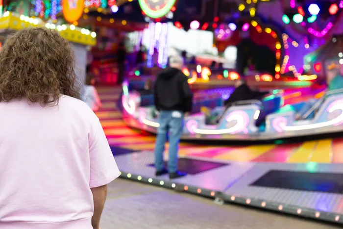 Rückansicht einer Person mit lockigem Haar vor einem bunten Karussell auf der Kirmes.
