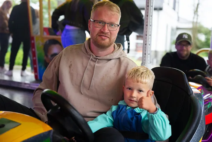 Ein Mann und ein kleiner Junge sitzen in Autoscootern auf der Kirmes. Der Junge zeigt mit dem Daumen nach oben.