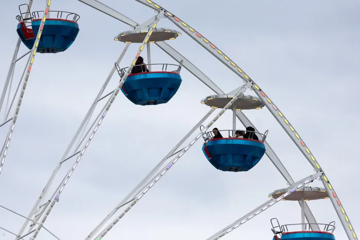 Riesenrad mit mehreren blauen Gondeln vor grauem Himmel, einige mit Fahrgästen besetzt.