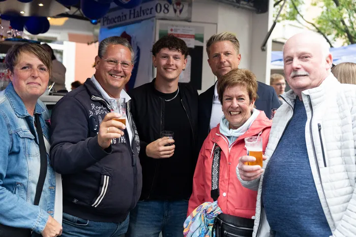 Sechs lächelnde Menschen stehen eng zusammen und halten Biergläser in der Hand, im Hintergrund ein Kirmeszelt mit dem Schriftzug „Phoenix Halver 08“.