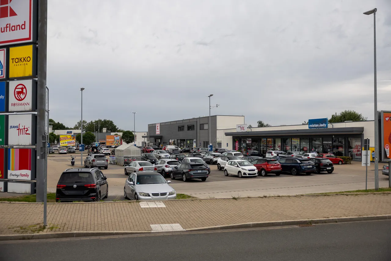 Ein Parkplatz mit zahlreichen Autos vor den Ladenfronten des Fachmarktzentrums Halver unter bewölktem Himmel.