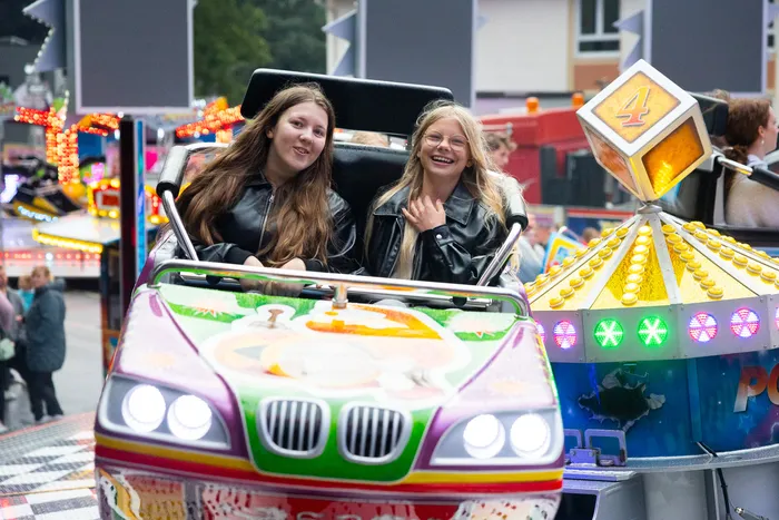 Zwei junge Frauen lachen in einem bunt beleuchteten Karussellfahrzeug auf der Kirmes.