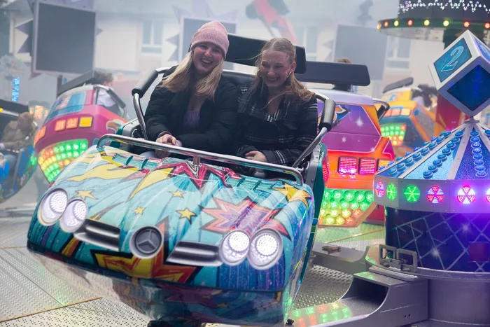 Zwei junge Frauen lachen während einer Fahrt mit einem bunt bemalten Autoscooter auf der Kirmes.