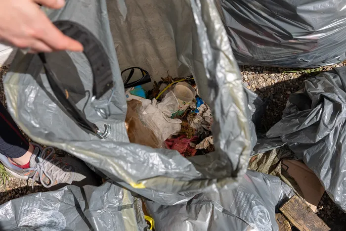 Ein grauer Müllsack, gefüllt mit Abfällen wie Papier und Blättern, steht auf einem Kiesuntergrund.