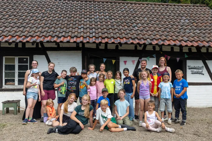 Eine Gruppe von Kindern und Erwachsenen posiert für ein Gruppenfoto vor einem weißen Gebäude mit Ziegeldach.