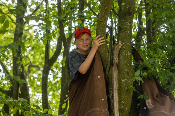Ein lächelnder Junge mit roter Kappe steht in einem Wald.