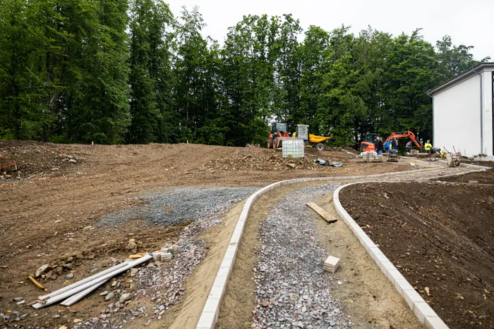 Bauarbeiten auf dem Gelände der Grundschule auf der Wahr in Meinerzhagen. Im Vordergrund eine neu angelegte Wegefläche, im Hintergrund schwere Baumaschinen und Arbeiter.