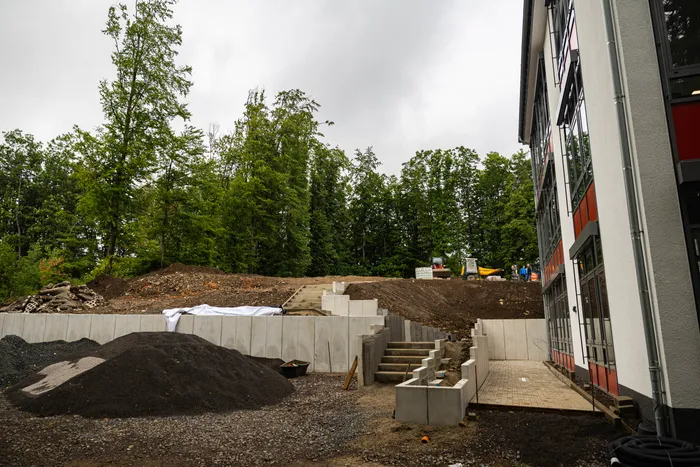 Baustelle auf dem Gelände der Grundschule auf der Wahr in Meinerzhagen: Eine Rampe und Treppenstufen werden in eine Hanglage gebaut, davor liegt ein großer Schotterhaufen. Im Hintergrund ein dichter Wald.