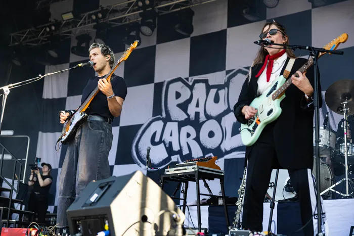 Paula Carolina singt und spielt eine hellblaue E-Gitarre auf der Bühne des Bautz-Festivals vor einem schwarz-weiß karierten Hintergrund.