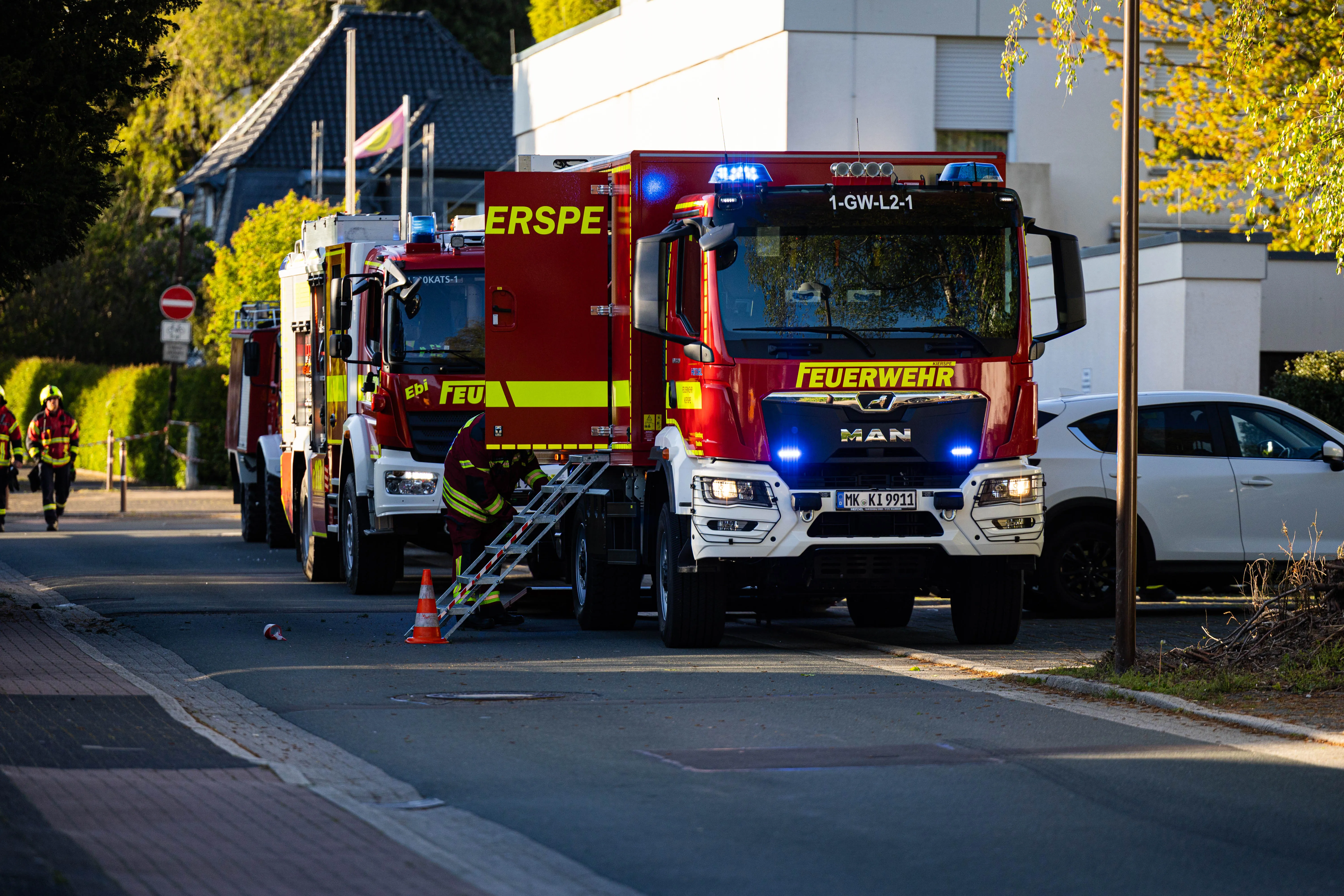 Mehrere rote Feuerwehrautos stehen auf einer Straße vor einem Wohnhaus, während Einsatzkräfte einen Brand bekämpfen.