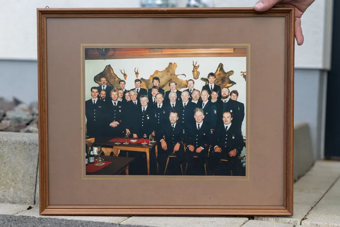 Eine Gruppe von etwa 30 Männern in dunklen Uniformen posiert für ein Gruppenfoto. Im Hintergrund sind Tierköpfe an der Wand zu sehen.
