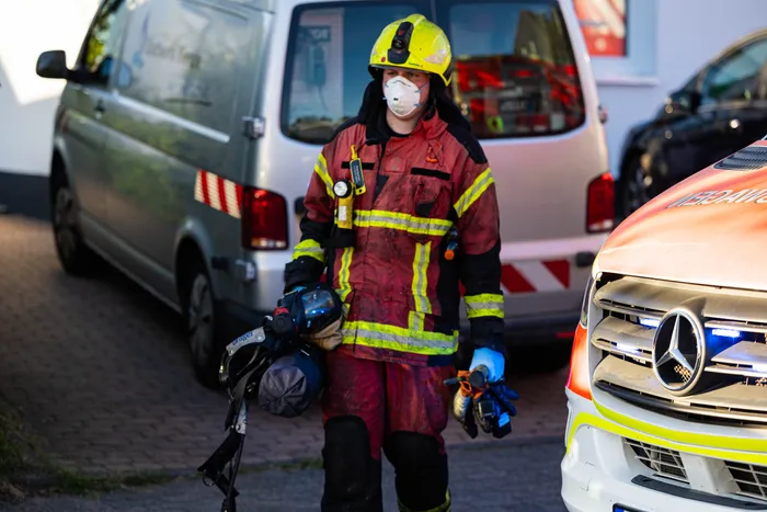 Feuerwehrmann in voller Schutzausrüstung steht vor Einsatzfahrzeugen nach einem Wohnungsbrand in Kierspe.