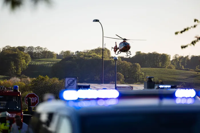 Ein Rettungshubschrauber landet auf einer Autobahn neben Einsatzfahrzeugen mit Blaulicht, während im Hintergrund Bäume und Hügel zu sehen sind.