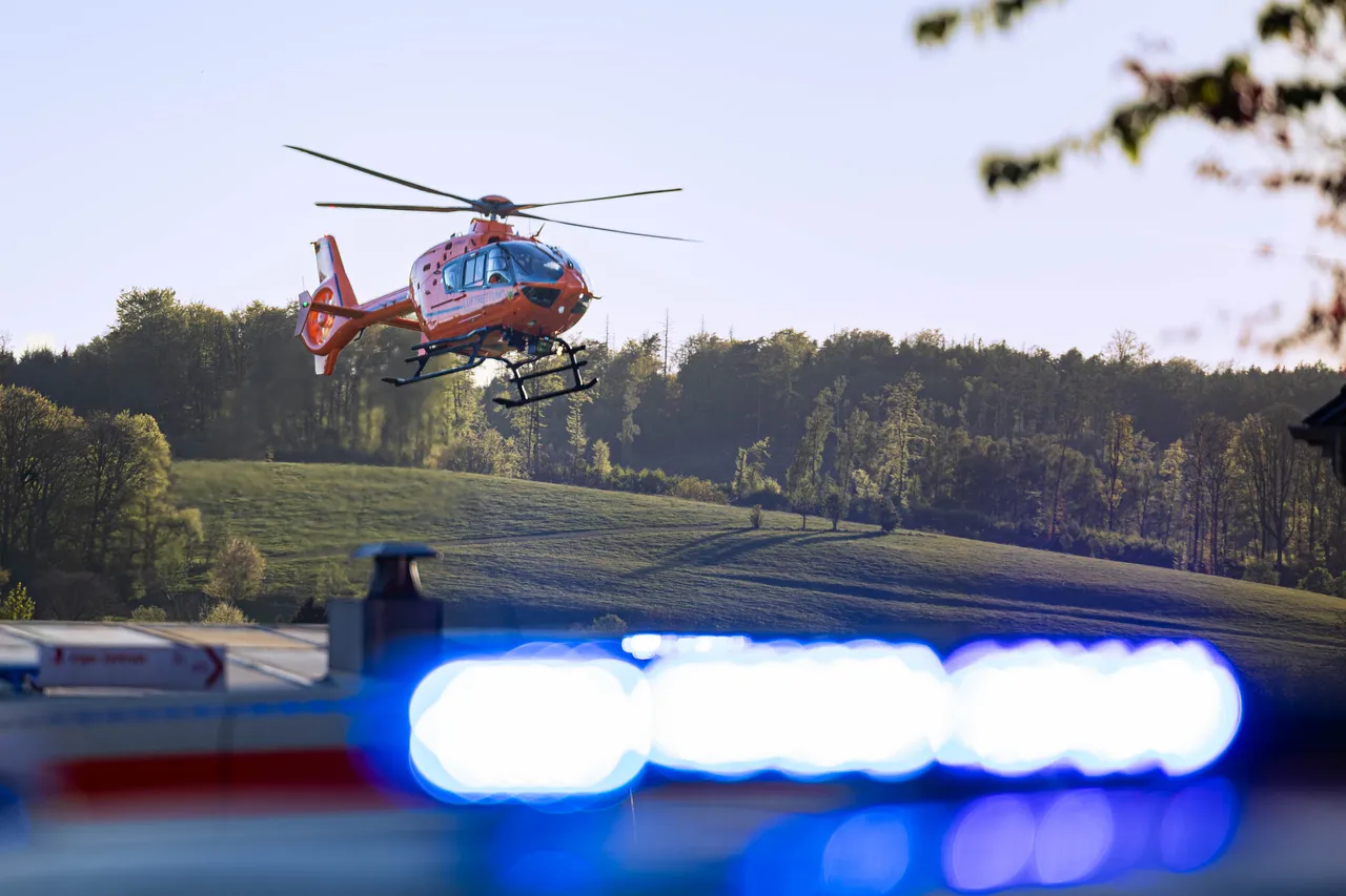 Rettungshubschrauber im Flug über einer Wiese, im Vordergrund Blaulicht. Symbolbild für Notfallrettung und Zivilschutz.