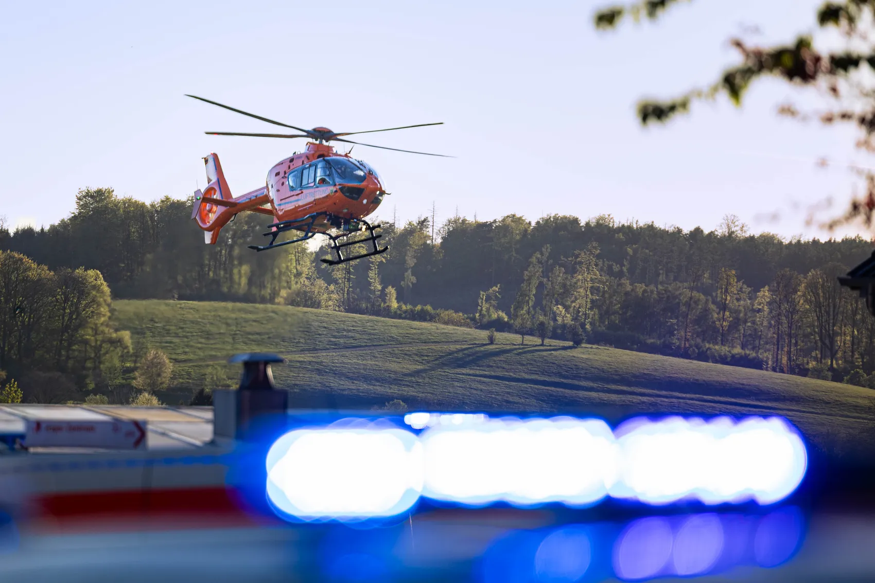 Rettungshubschrauber im Flug über einer Wiese, im Vordergrund Blaulicht. Symbolbild für Notfallrettung und Zivilschutz.