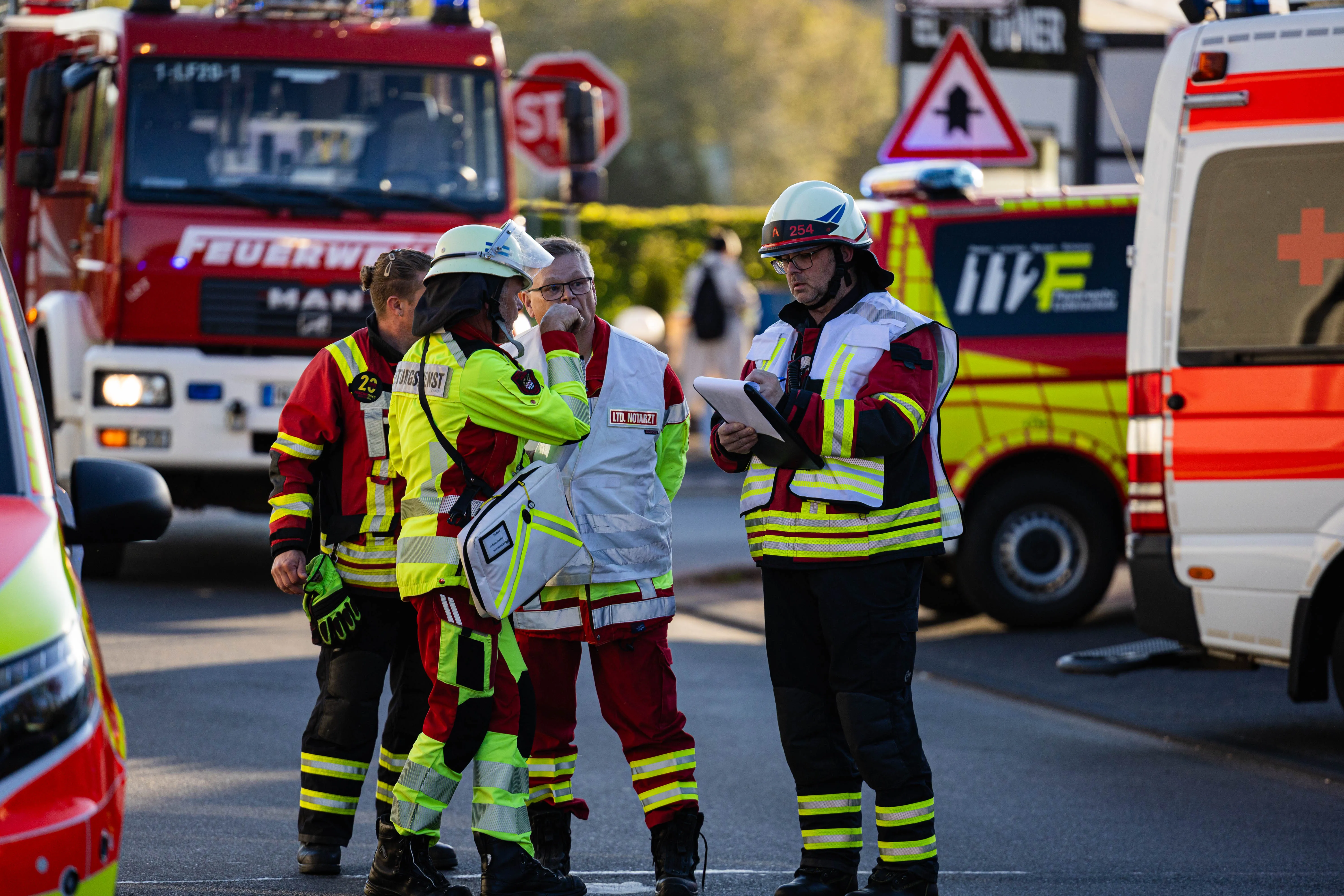 Mehrere Einsatzkräfte in voller Montur besprechen sich auf einer Straße vor einem Feuerwehrauto und einem Rettungswagen nach einem Brand in Kierspe.
