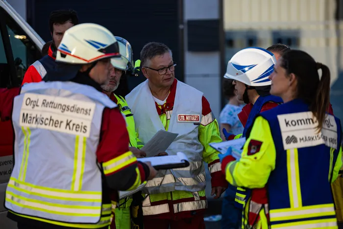 Ein Notarzt bespricht mit Feuerwehrleuten den Einsatzort eines Wohnungsbrandes, während eine weitere Einsatzkraft Notizen macht.