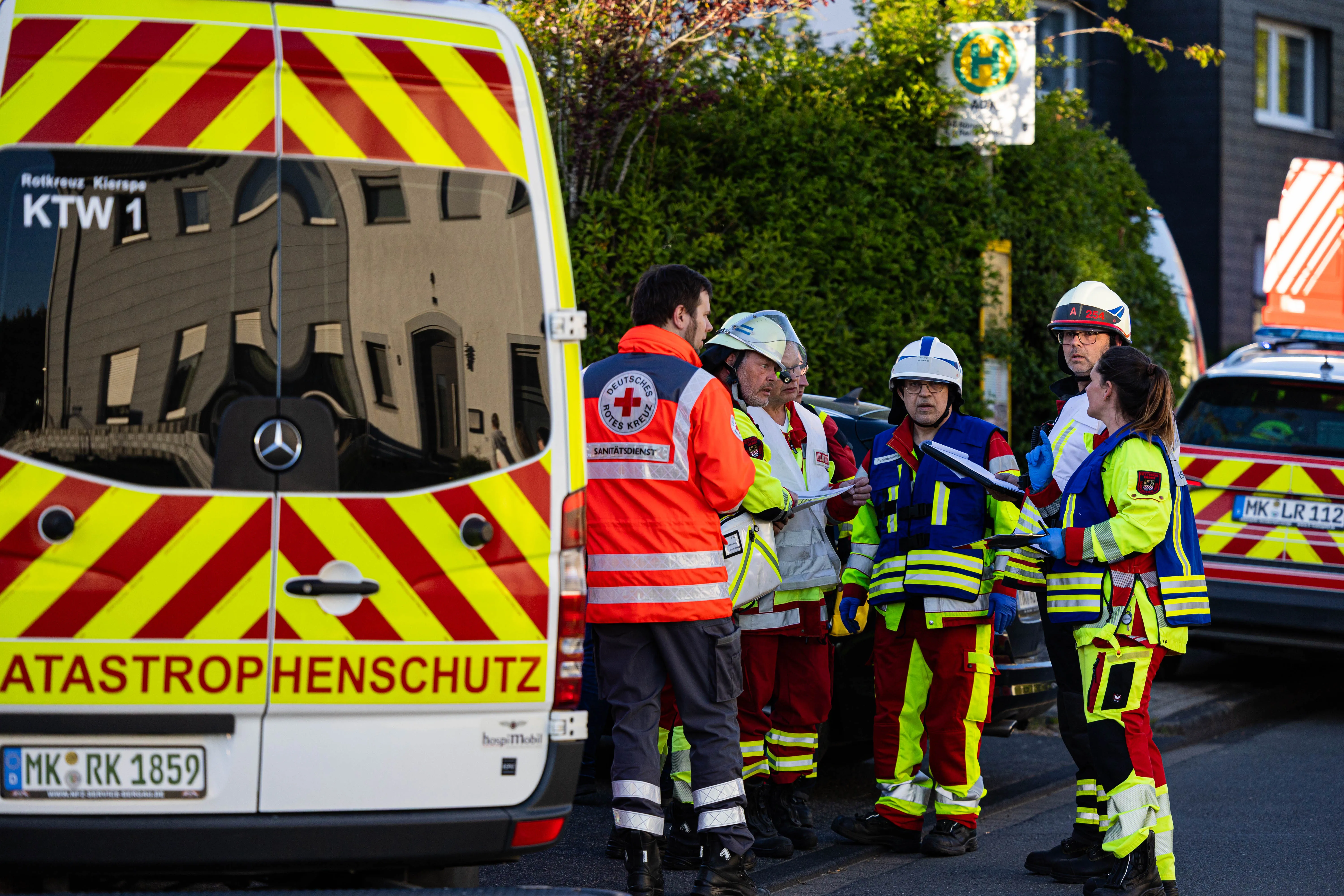 Rettungskräfte in gelben Westen stehen vor einem Rettungswagen mit der Aufschrift „Katastrophenschutz“ nach einem Wohnungsbrand in Kierspe.