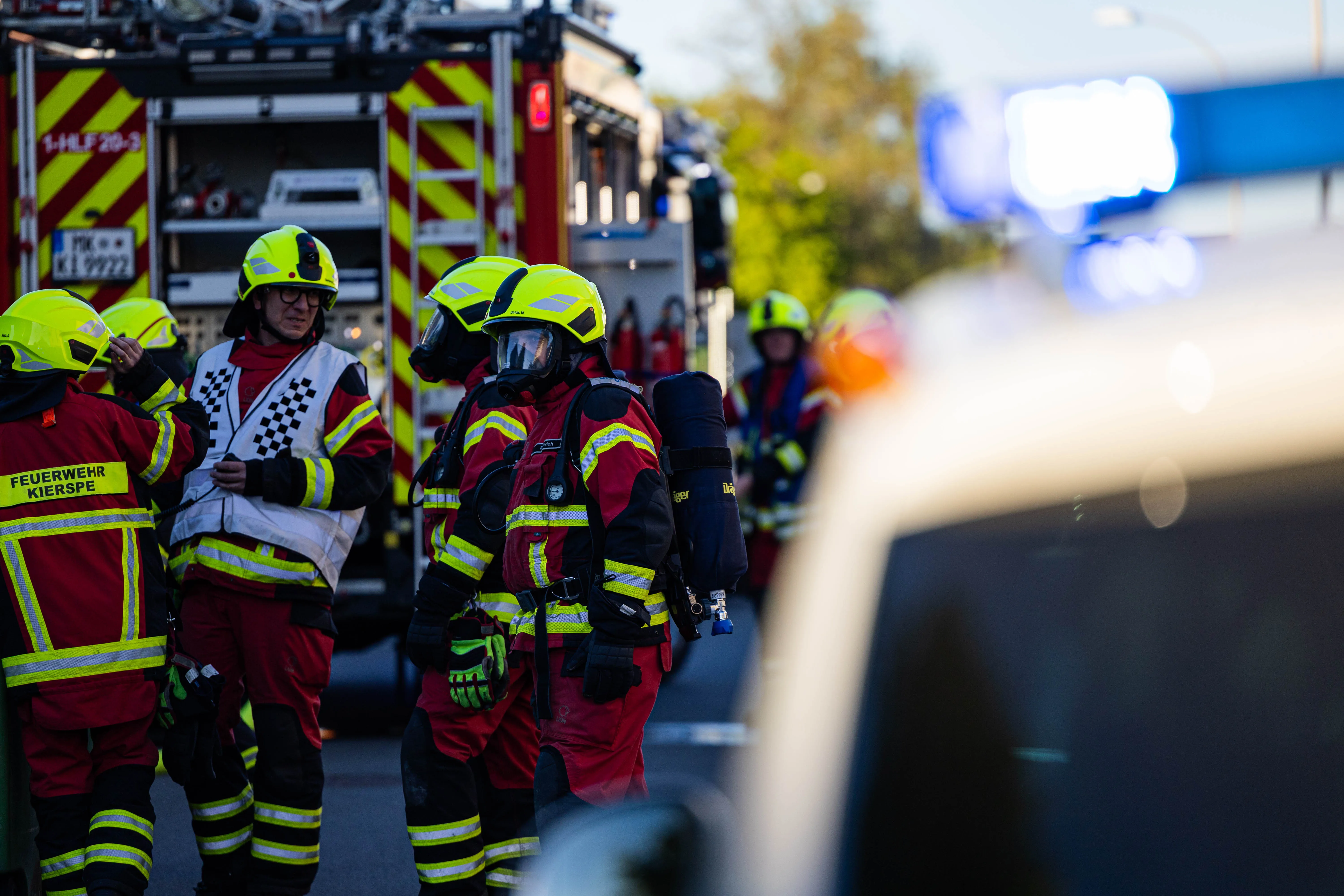 Feuerwehrleute in voller Montur stehen vor einem Feuerwehrauto während eines Einsatzes bei einem Wohnungsbrand in Kierspe.