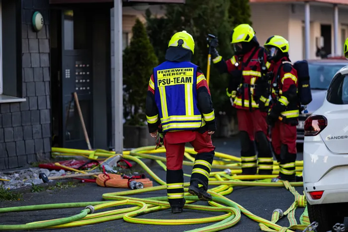 Feuerwehrleute in Kierspe bei der Brandbekämpfung, Schläuche liegen auf dem Boden vor einem Wohnhaus.