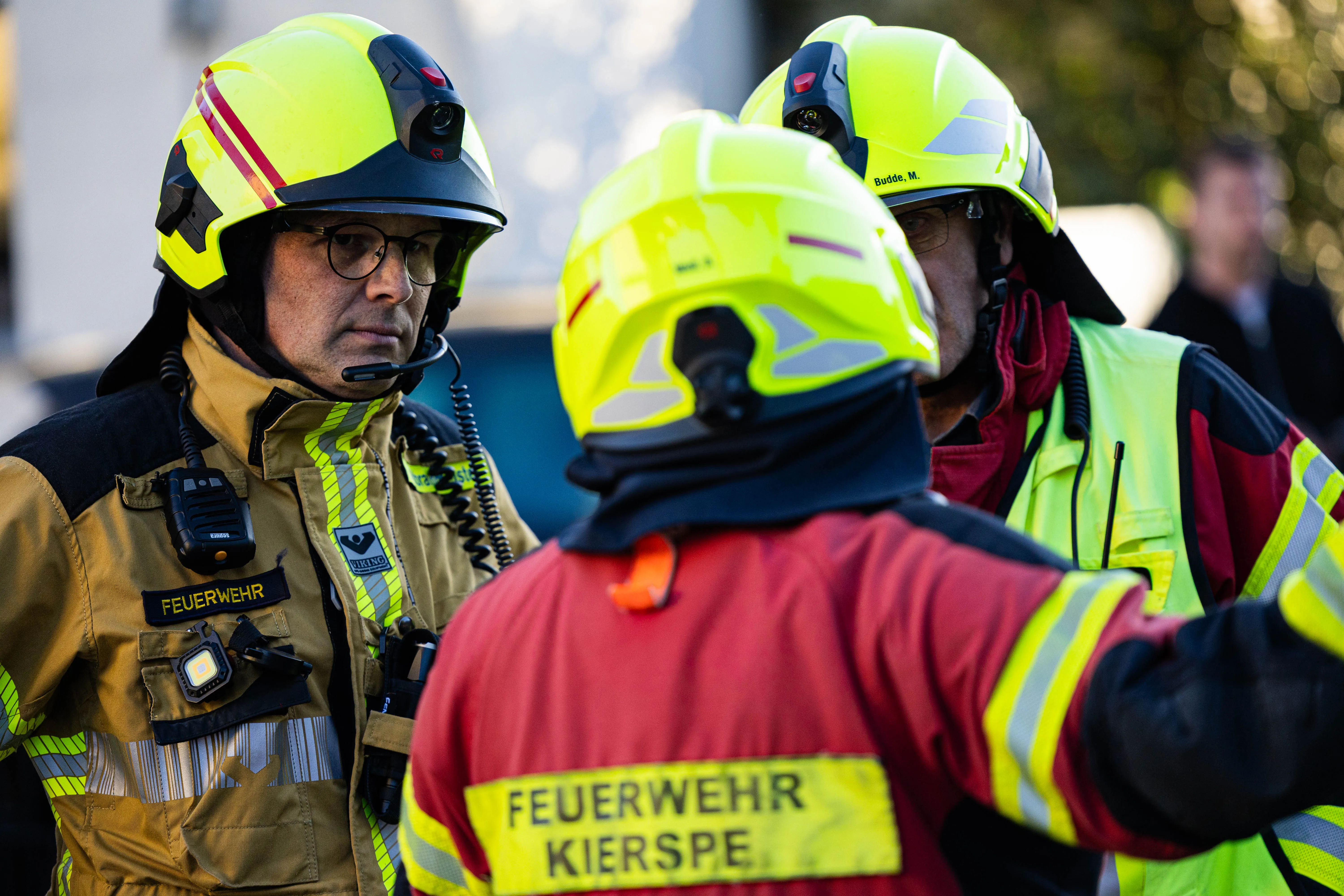 Feuerwehrleute mit Schutzhelmen und Funkgeräten besprechen während eines Einsatzes in Kierspe die Lage nach einem tödlichen Wohnungsbrand.