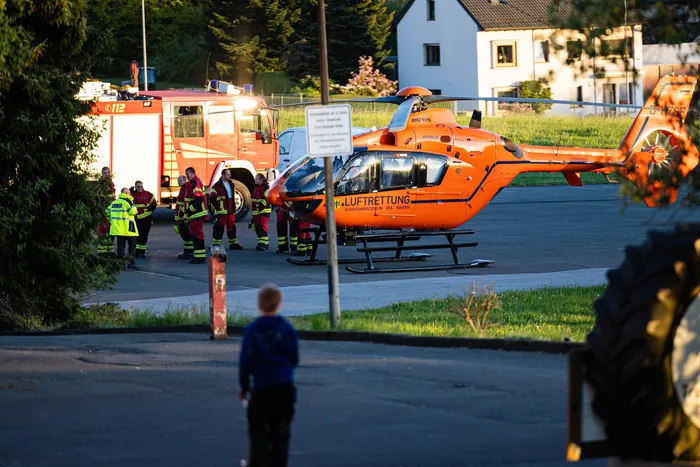 Rettungskräfte stehen um einen orangefarbenen Rettungshubschrauber und einen roten Feuerwehrauto nach einem Wohnungsbrand. Im Vordergrund ist ein Kind zu sehen.