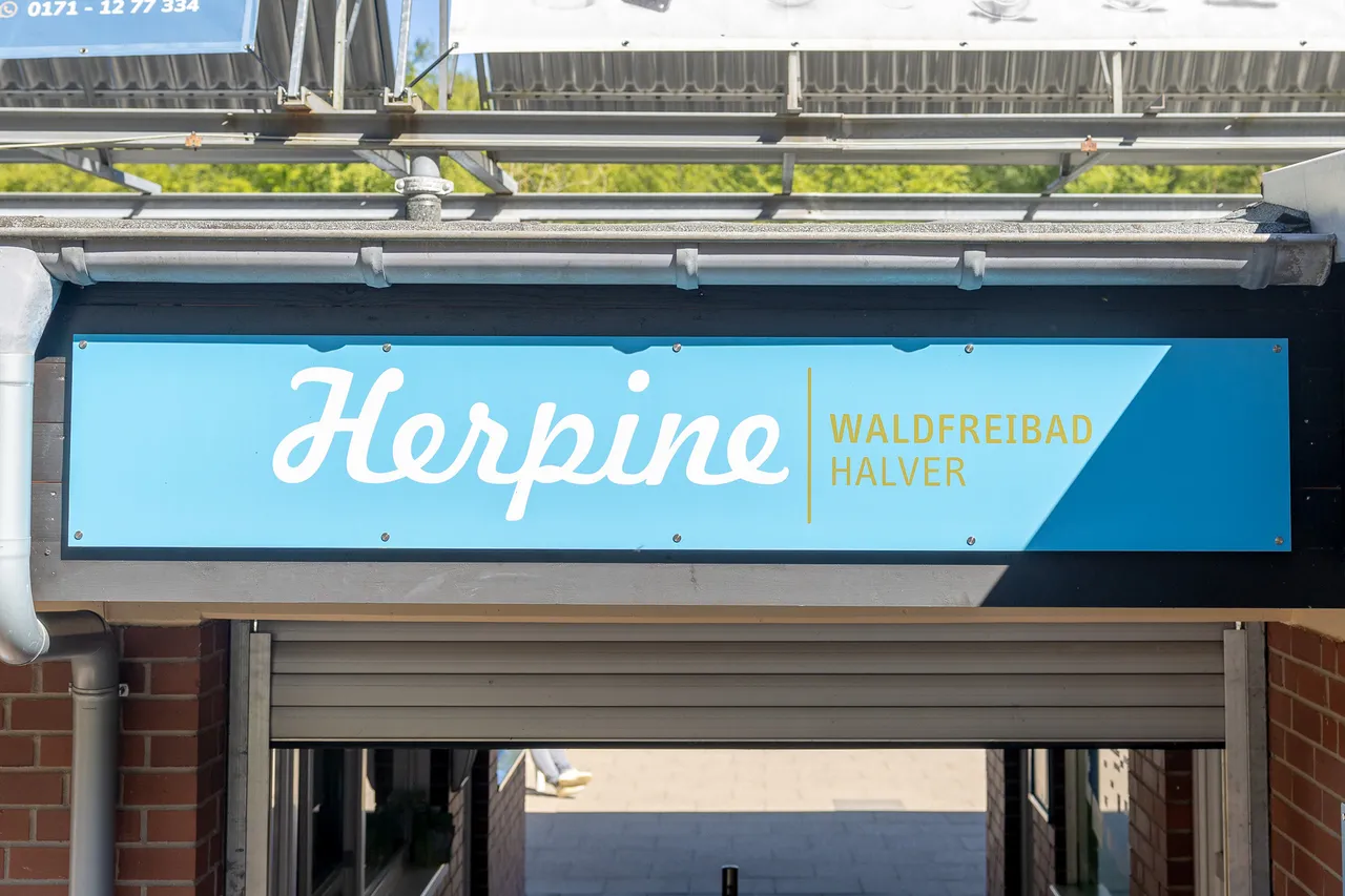 Blaues Schild mit dem Schriftzug „Herpine Waldfreibad Halver“ über einem Rolltor.