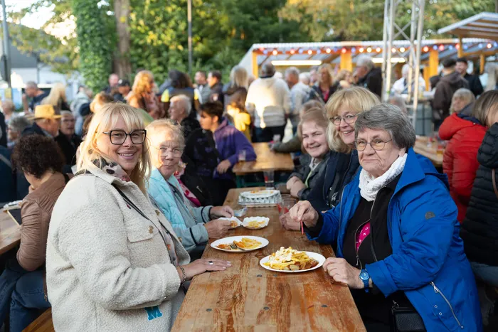 Eine Gruppe von Menschen, vor allem ältere Frauen, sitzt an Holztischen und isst bei einem Gemeindefest im Freien.